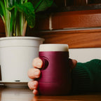 Bicchiere intelligente Drinky rosso e bianco, vista frontale in ambiente domestico, impugnato da una mano e posato su un tavolo.