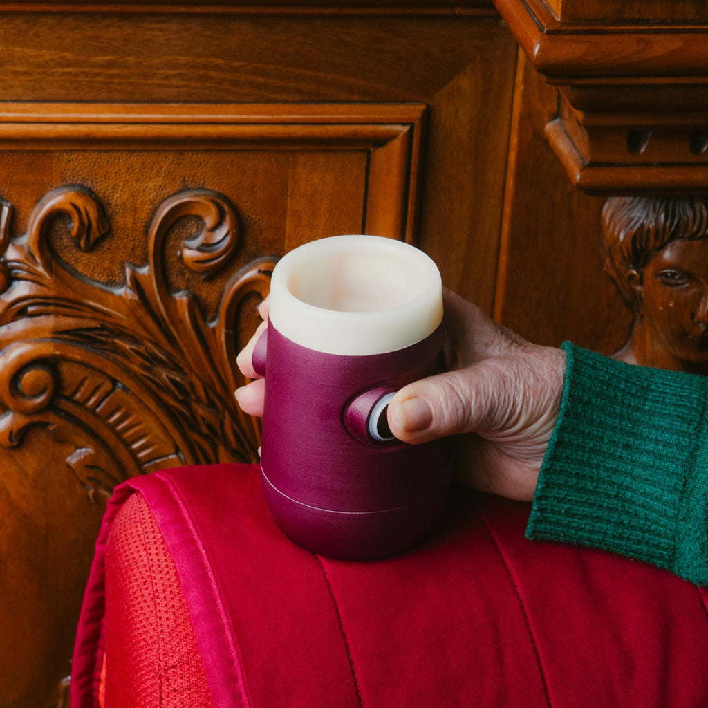 Bicchiere intelligente Drinky rosso e bianco, vista laterale in ambiente domestico, impugnato da una mano e posato sul bracciolo di un divano.
